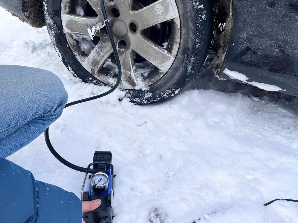 Close up of person checking a car's tyre pressure on a snowy day